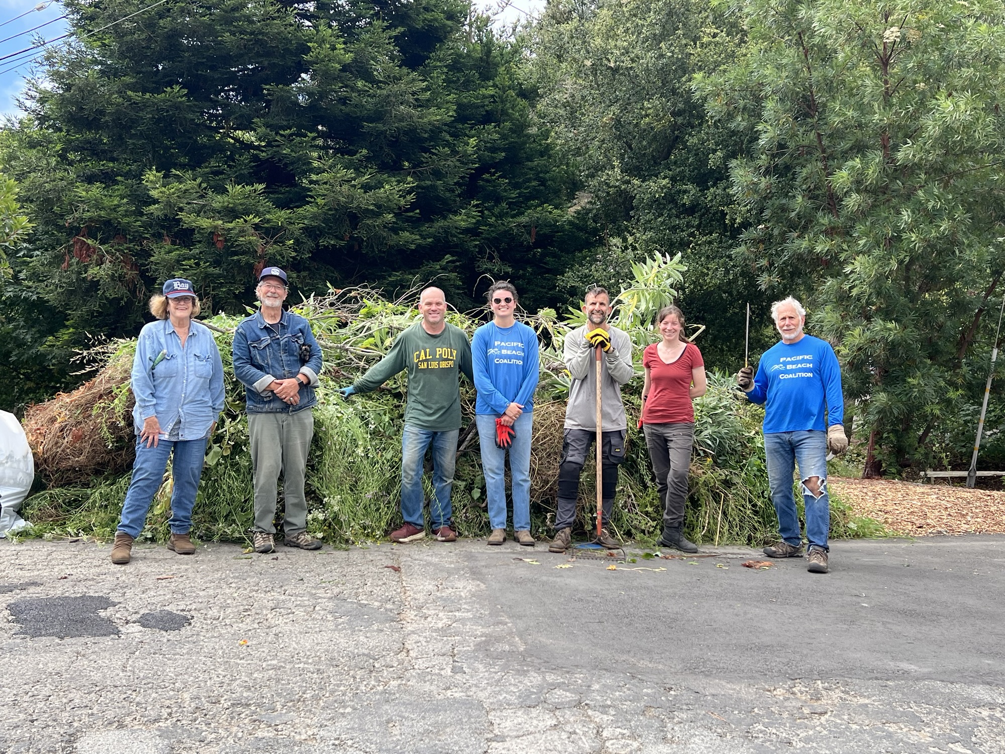 Volunteers stand in front of a pile of weeds