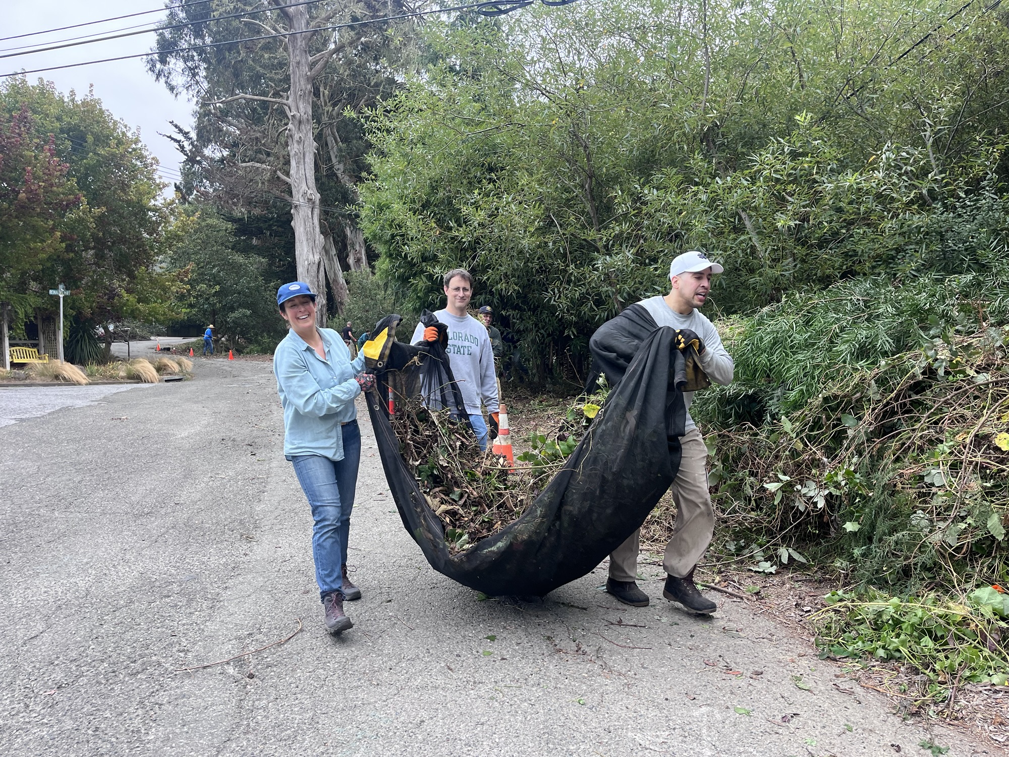 Three volunteers carry a tarp full of weeds